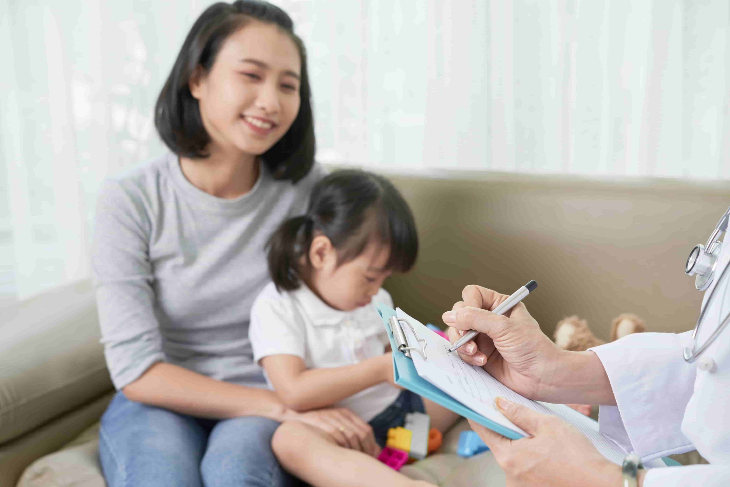 A mother and young child attending an NDIS speech pathology assessment with a specialist taking notes on a clipboard.