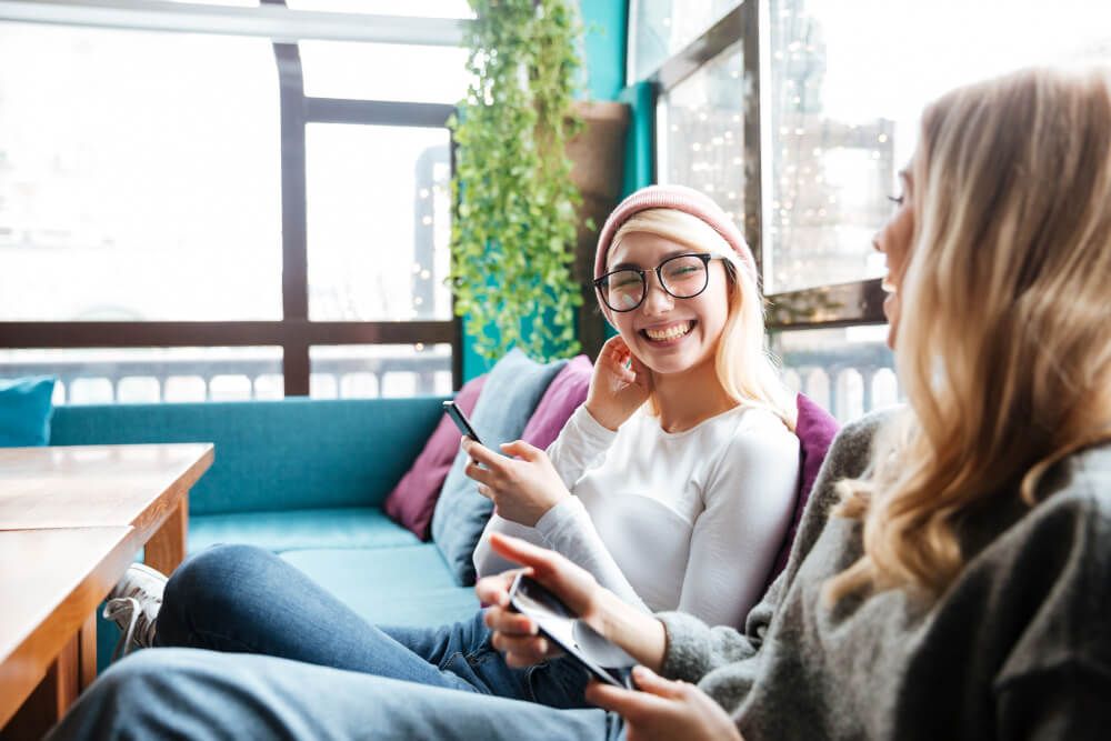 cheerful women using cell phones and discussing